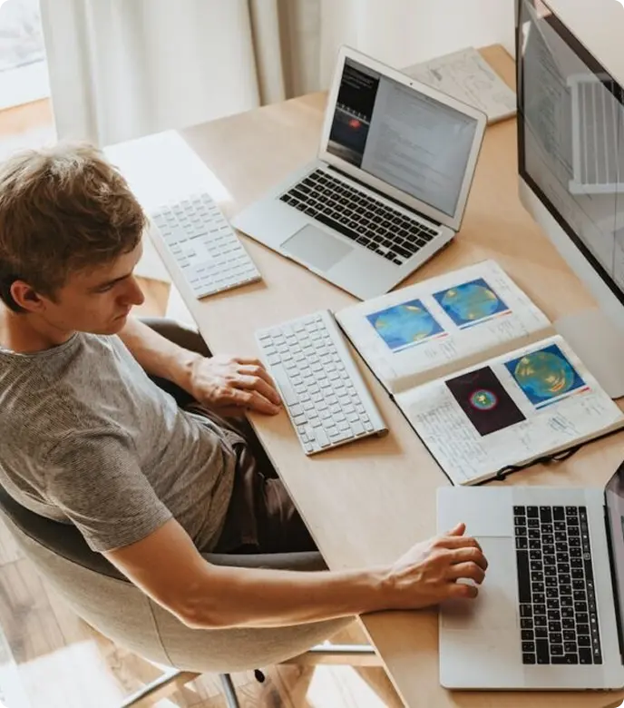 A man at a desk with two laptops and a computer